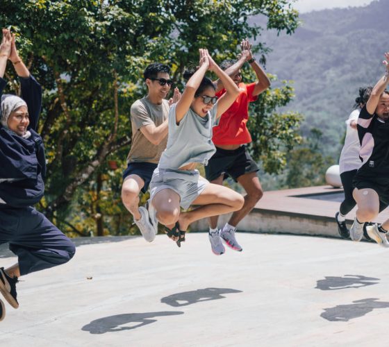 Puma team building participants jumping in sync with hands raised on an outdoor patio during a photo challenge at Hillcrest Dawn in Bentong